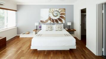 Un dormitorio moderno con una cama grande, suelo de madera, ventilador de techo y una obra de arte en la pared.