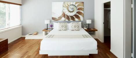 Un dormitorio moderno con una cama grande, suelo de madera, ventilador de techo y una obra de arte en la pared.