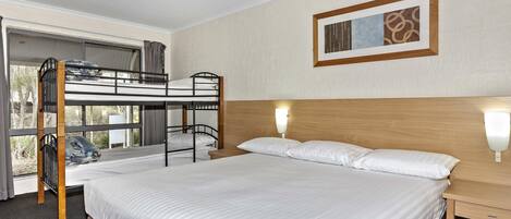 Una cama nido con cabecera de madera, una mesita de noche con lámpara, y un cuadro en la pared.