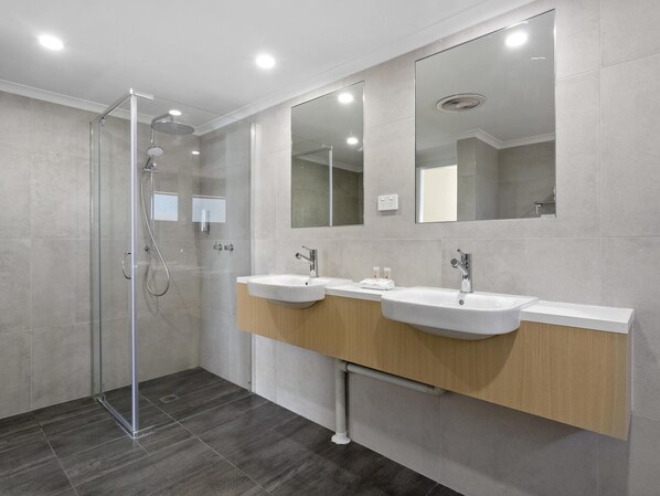 A modern bathroom with a glass shower enclosure, two sinks, and a large mirror. - ibis Styles Canberra Eaglehawk (Sutton)