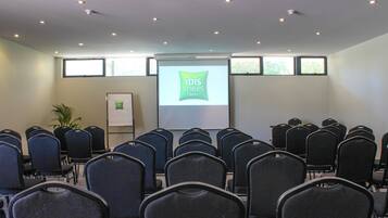 A conference room with rows of chairs facing a projection screen displaying 'ibis Styles Hotels'.
