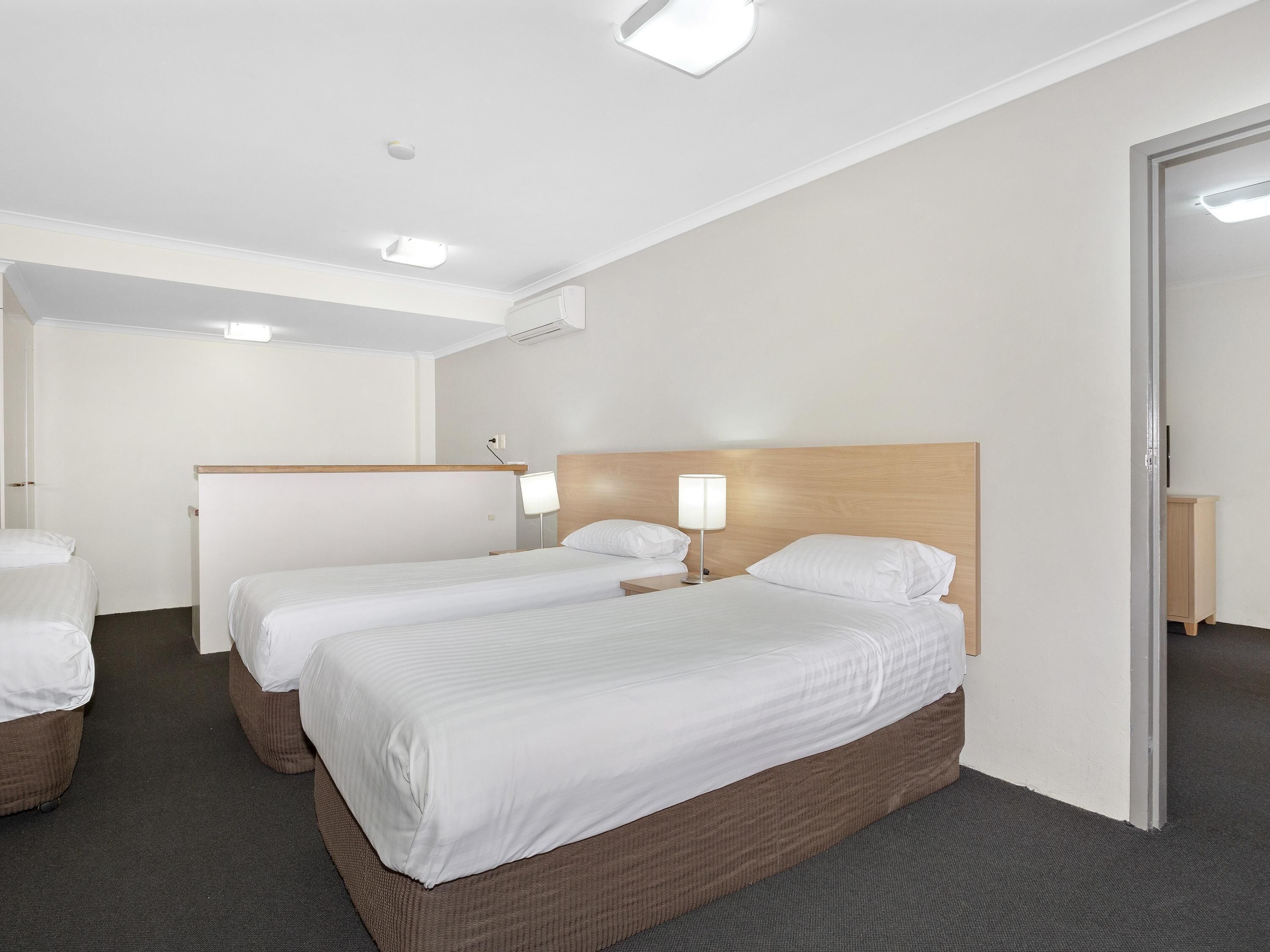 Ein Hotelzimmer mit zwei Einzelbetten, einem Holzkopfstück, einem Nachttisch mit Lampe und einem Kleiderschrank.