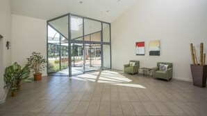 A spacious lobby with a modern glass partition, green seating, and potted plants. - ibis Styles Canberra Eaglehawk (Sutton)
