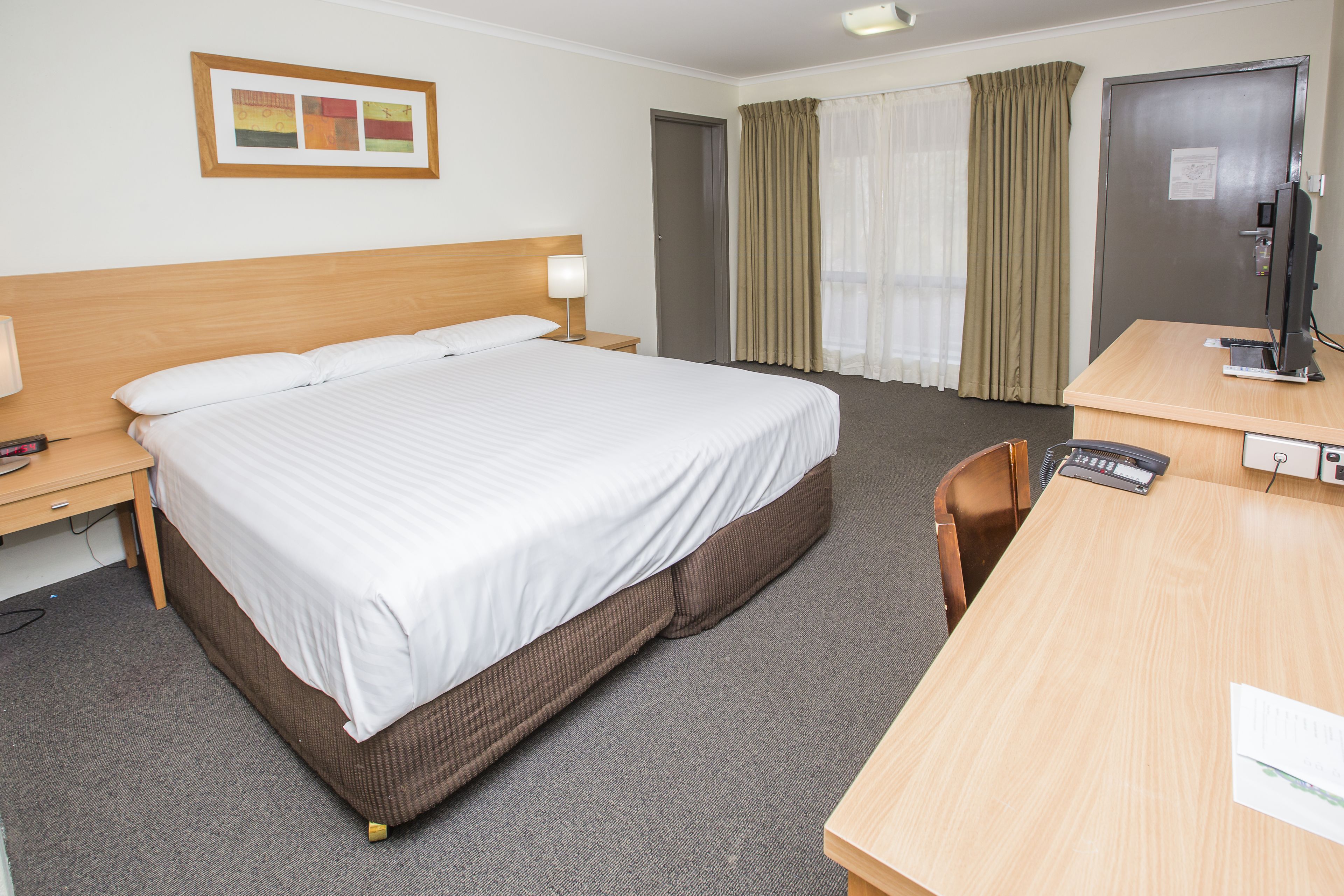 Quarto de hotel com uma cama grande, uma escrivaninha com computador e uma porta.