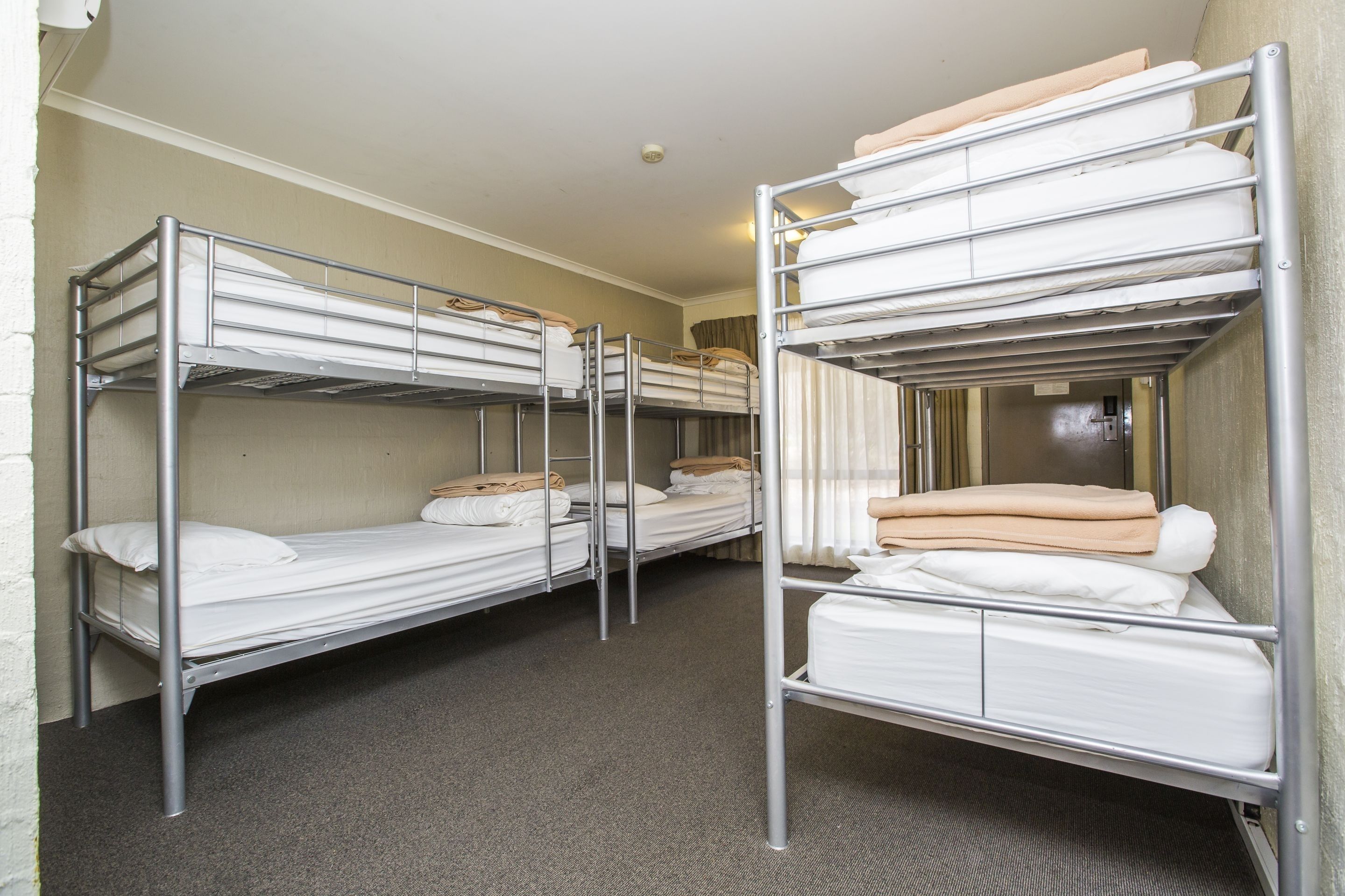 A room with bunk beds arranged in a row, each with a mattress and pillows.