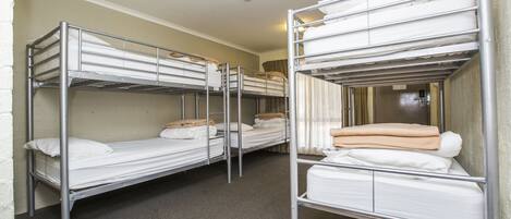 A room with bunk beds arranged in a row, each with a mattress and pillows.