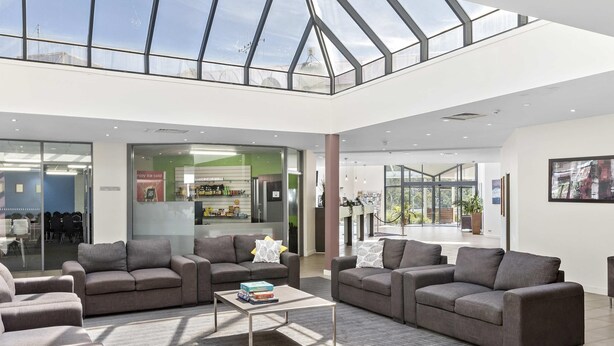 A spacious lobby with a high ceiling and skylight, modern furniture, and a visible kitchen area. - ibis Styles Canberra Eaglehawk (Sutton)