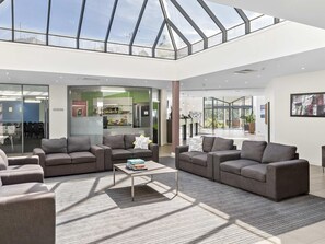A spacious lobby with a high ceiling and skylight, modern furniture, and a visible kitchen area. - ibis Styles Canberra Eaglehawk (Sutton)