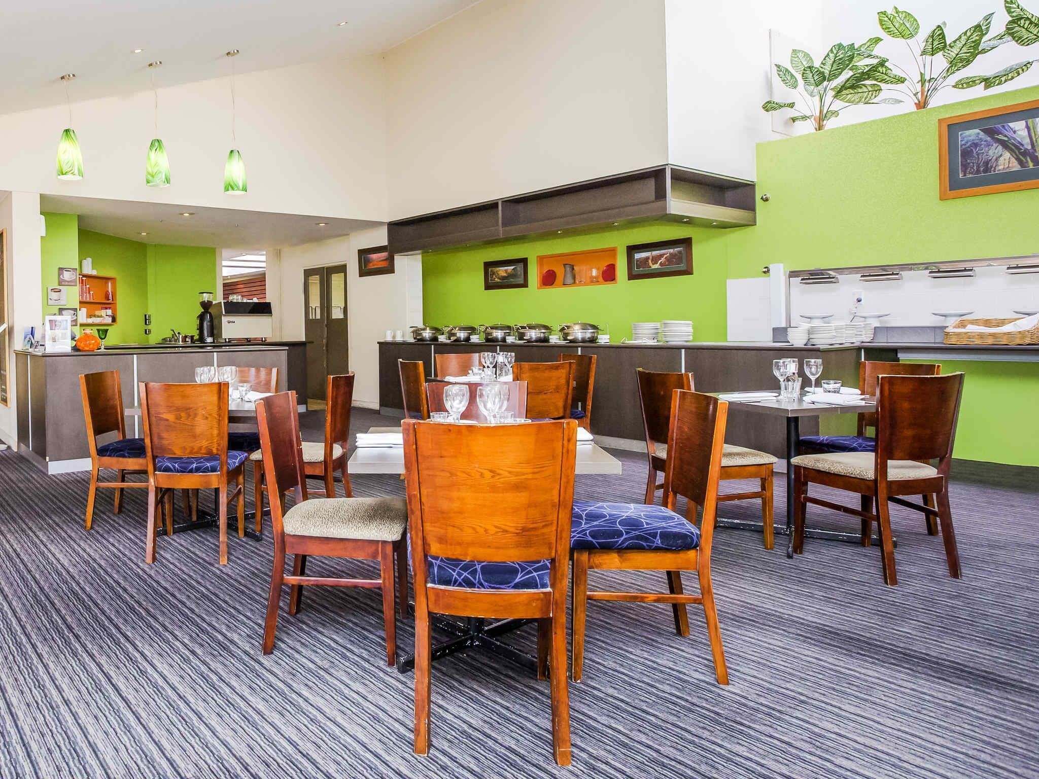 Un restaurante con sillas y mesas de madera, una pared verde y una barra con platos.