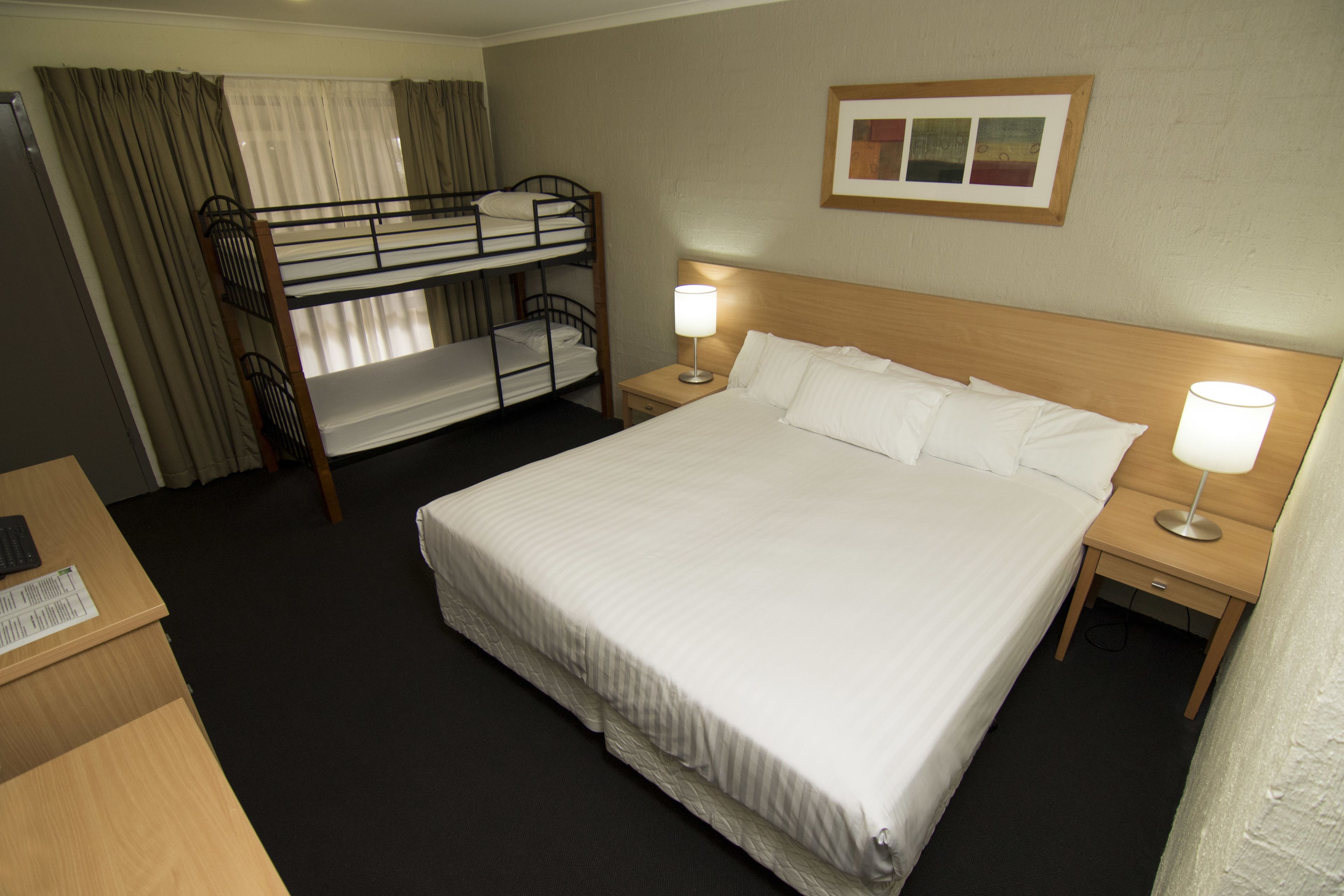 A hotel room with a single bed, a bunk bed, a desk, and a nightstand with lamps.