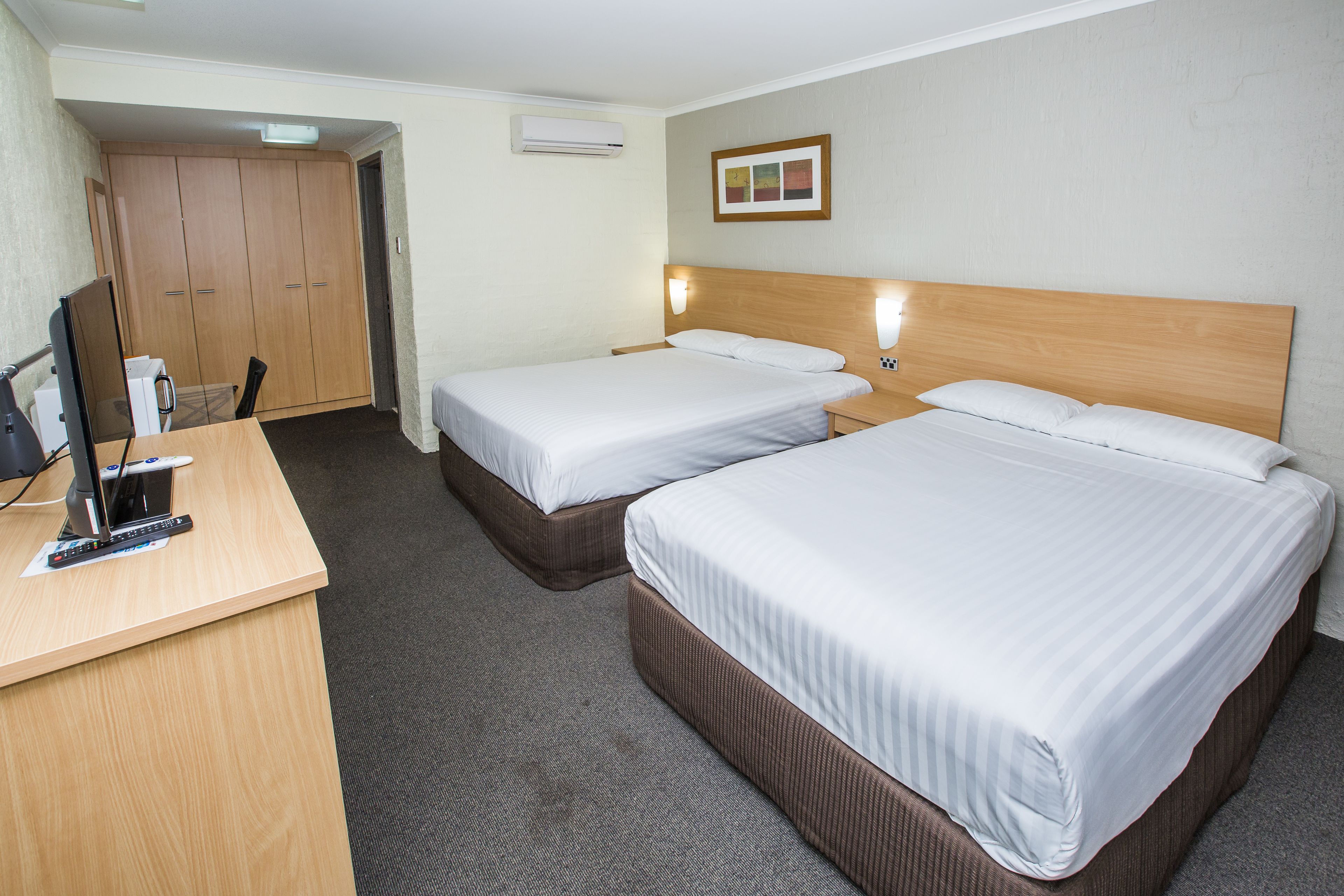 A hotel room with two beds, a desk with a computer, and a wardrobe.