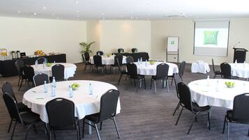 Un salón de conferencias con varias mesas, sillas y una pantalla para presentaciones.