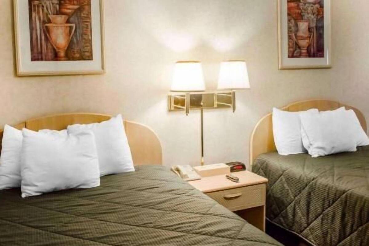 Una habitación de hotel con dos camas, una mesita de noche, una lámpara y dos cuadros en la pared.