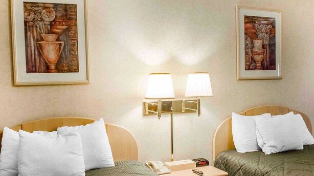 A hotel room with two single beds, a bedside table with a lamp, a nightstand, and two framed pictures on the wall.