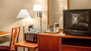 A hotel room with a wooden desk, a television, a microwave, a chair, a lamp, and a mirror.