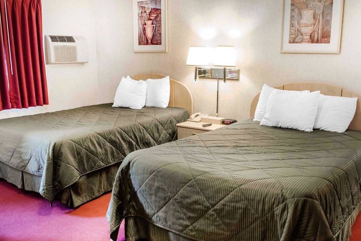 Habitación de hotel con dos camas, una mesita de noche con lámpara, teléfono y aire acondicionado instalado en la pared.