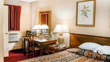 Una habitación de hotel con una cama, un escritorio con dos lámparas, un teléfono, una silla y un ventanal con cortinas.