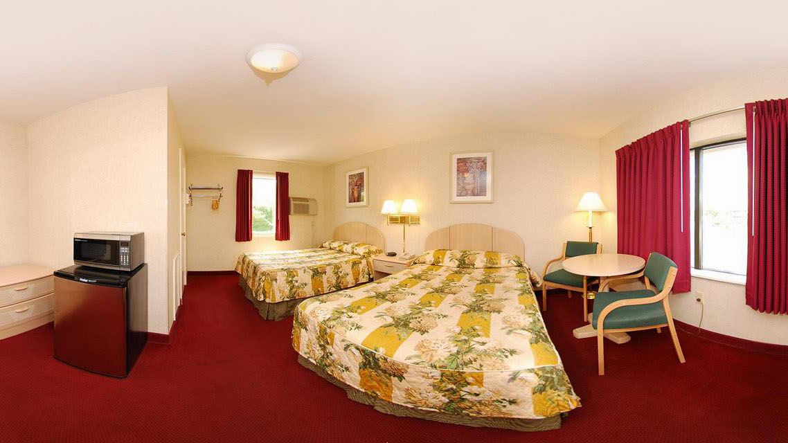 A hotel room with two beds, a desk, a chair, a microwave, and a window with curtains.