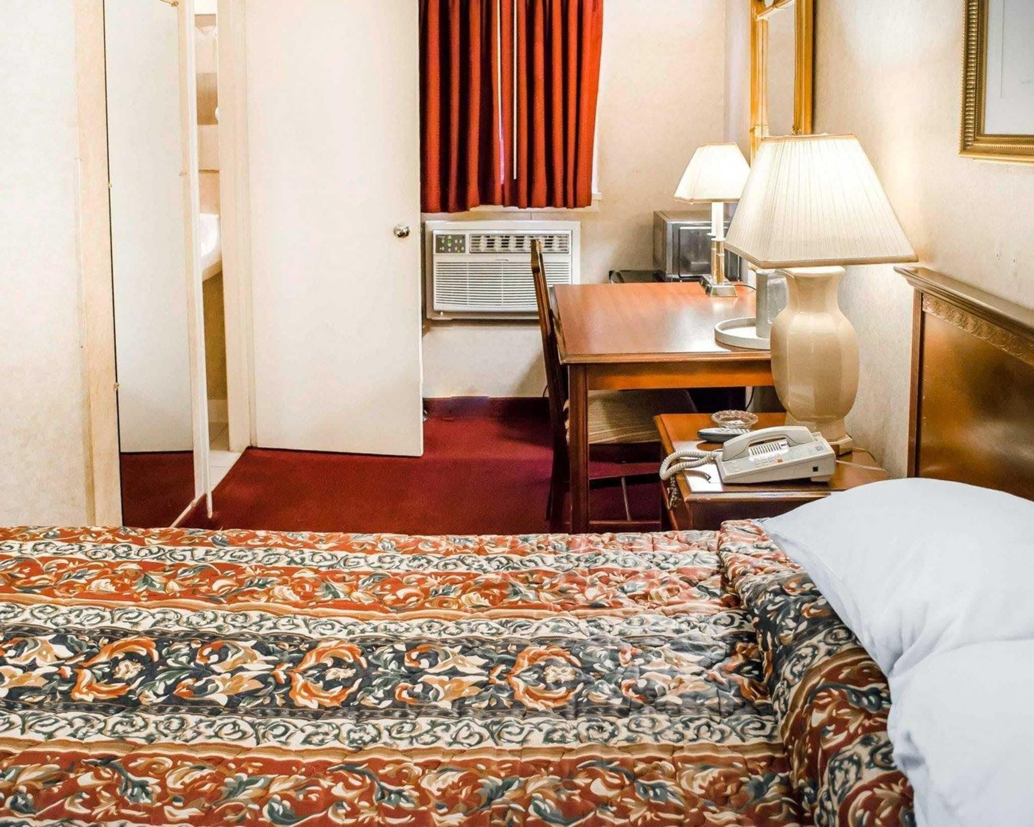 A hotel room with a bed, a desk, a telephone, a lamp, and a window with curtains.