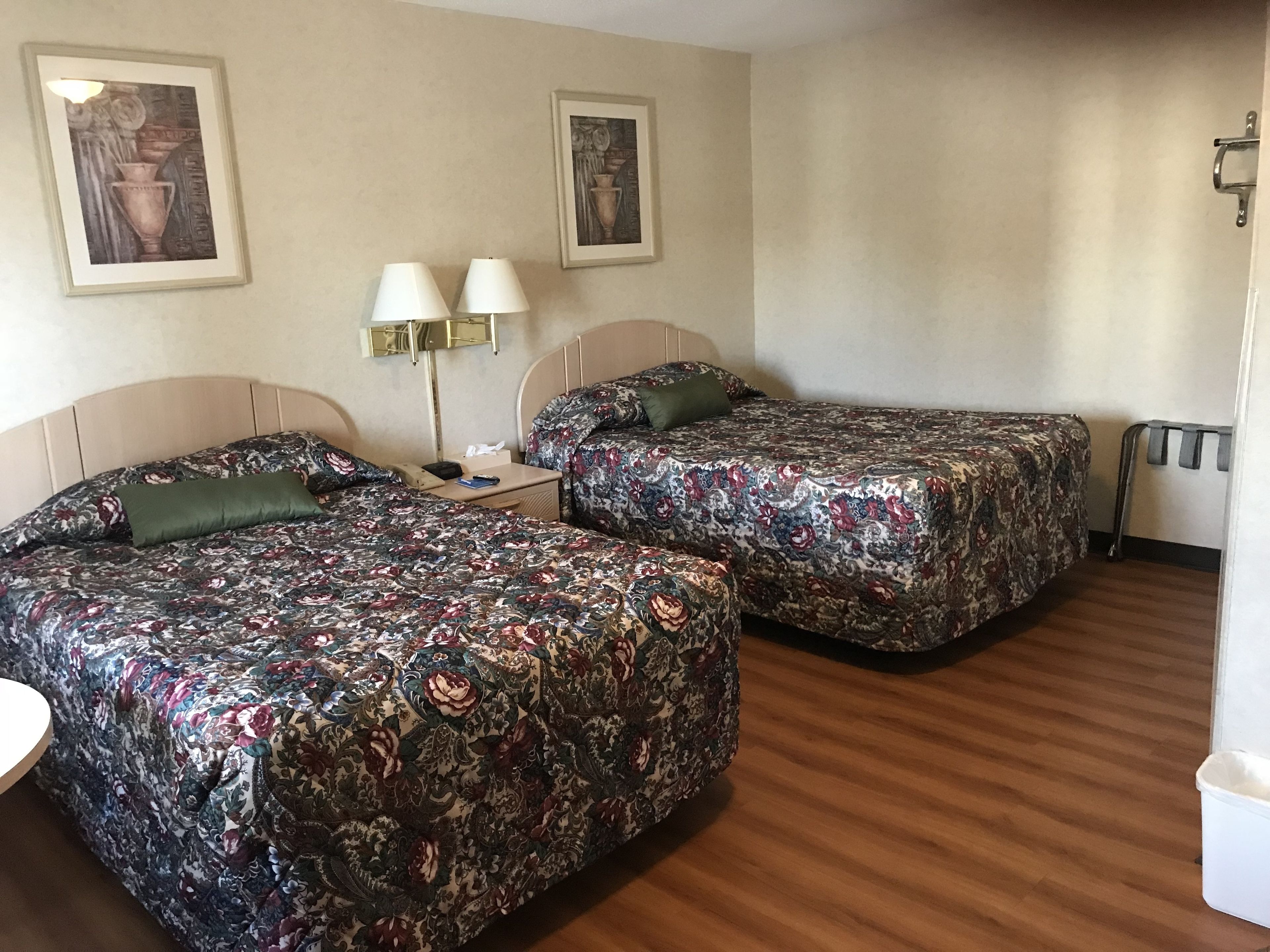 Een hotelkamer met twee bedden, een nachtkastje met lampen en twee ingelijste foto's aan de muur.