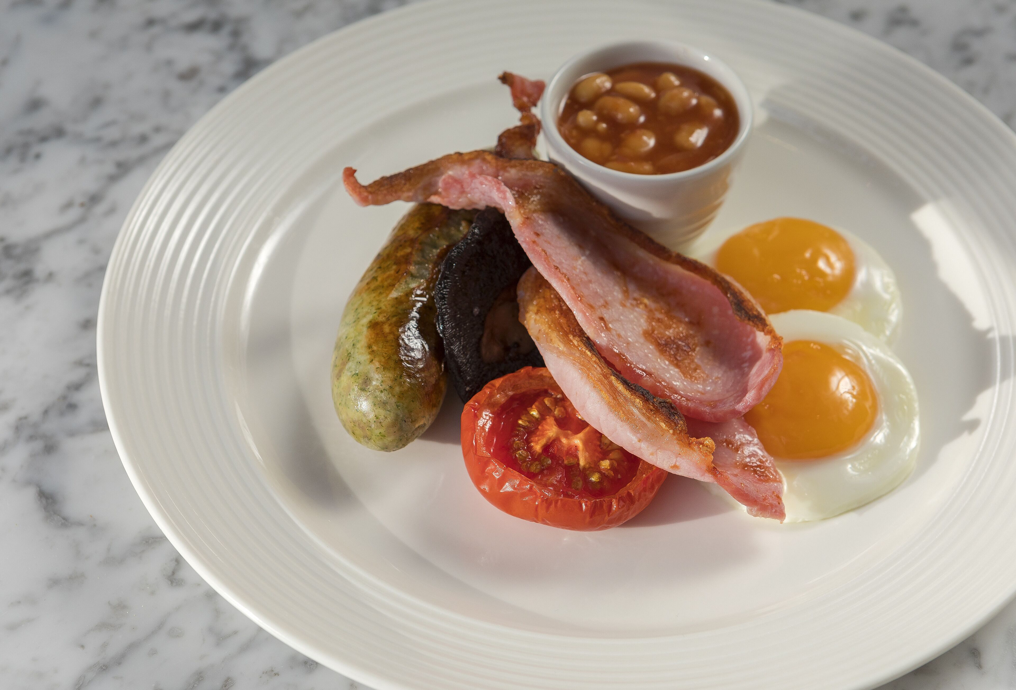 A plate with bacon, eggs, beans, and sausages.
