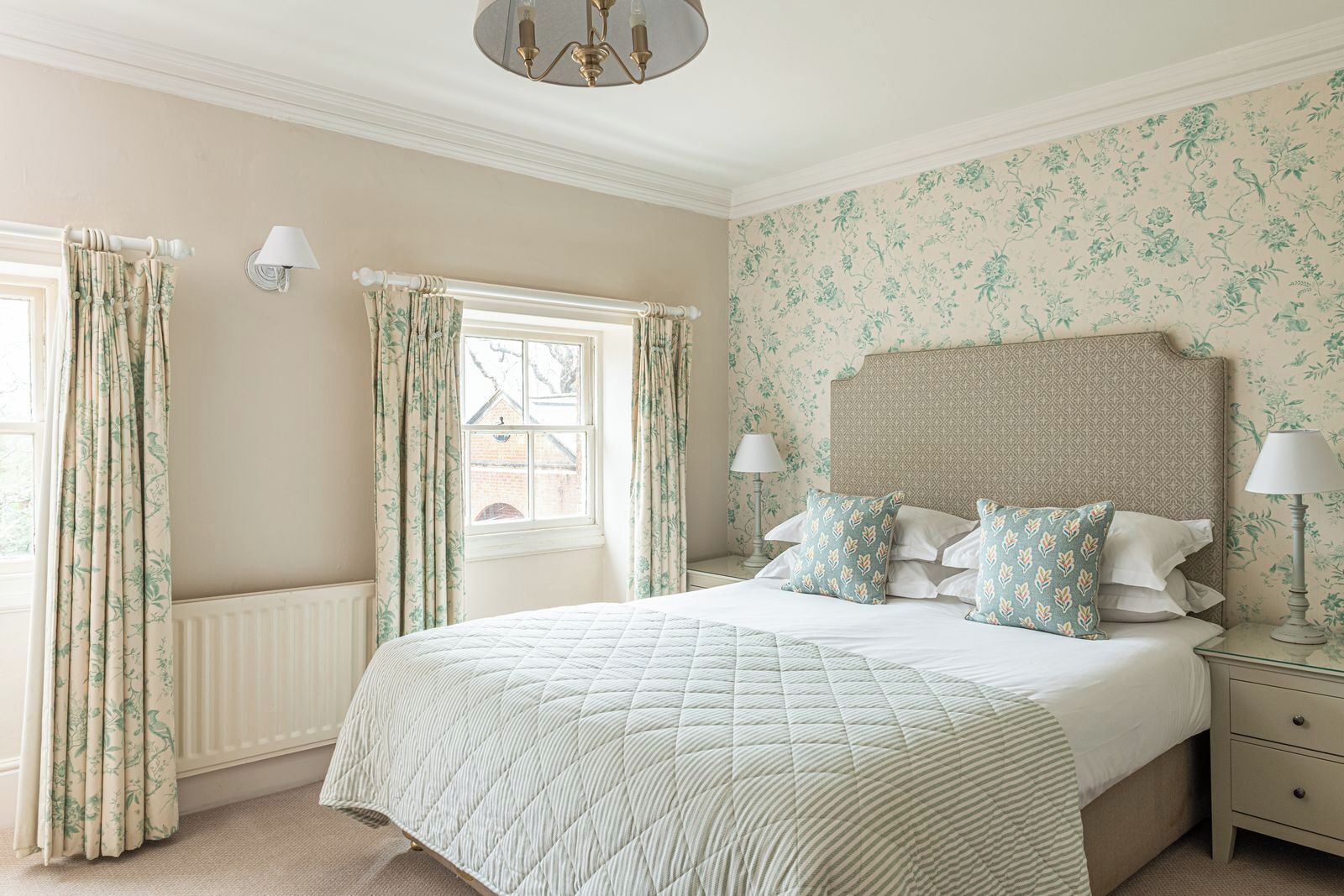 A bedroom with a large bed, floral wallpaper, and a window with curtains.