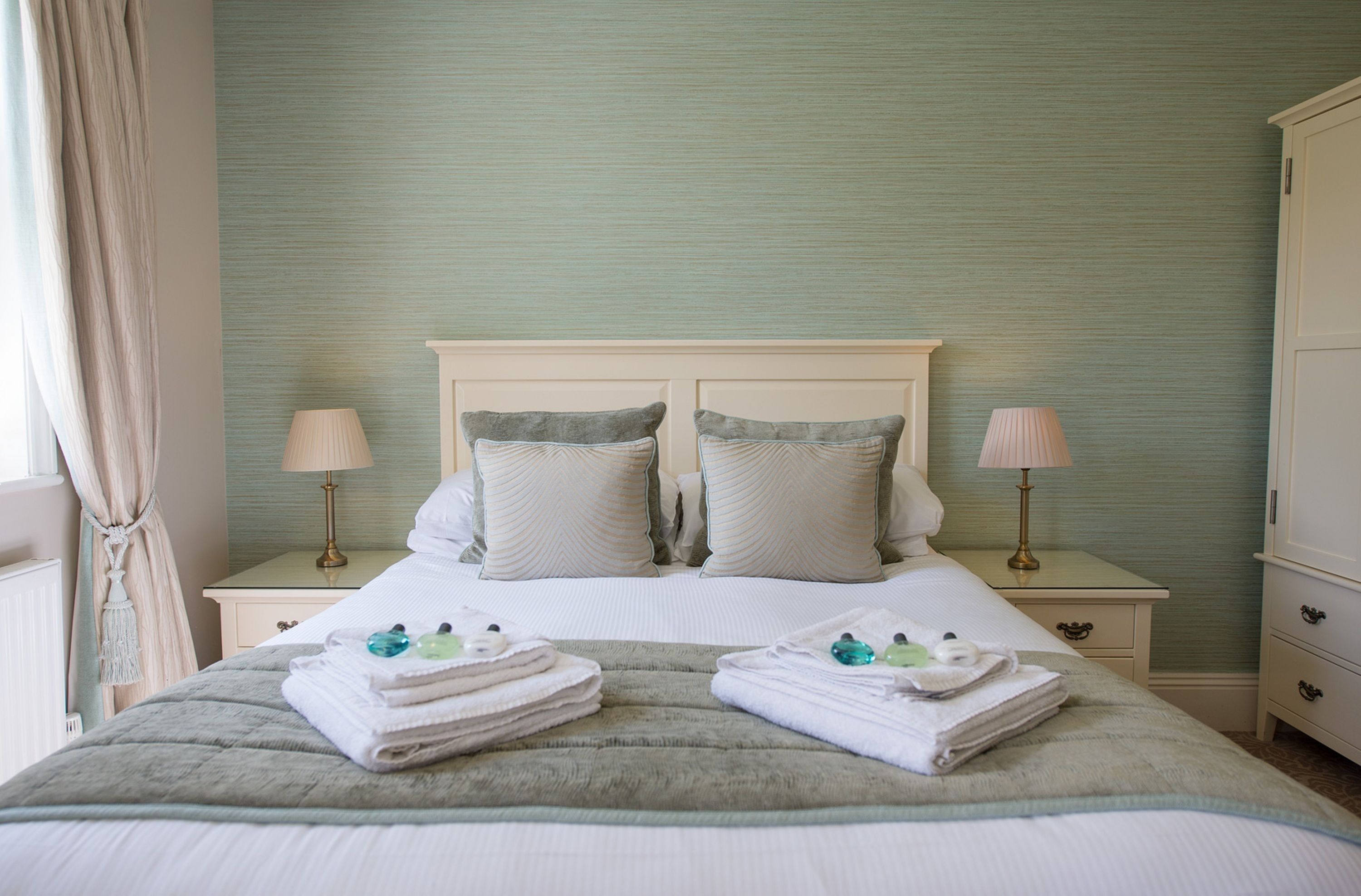 A neatly made bed with two pillows, a bedside table with a lamp, and a folded towel on the bed.