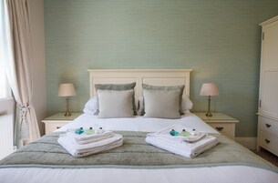 Una cama bien hecha con dos almohadas, una mesita de noche con una lámpara y una toalla doblada sobre la cama.
