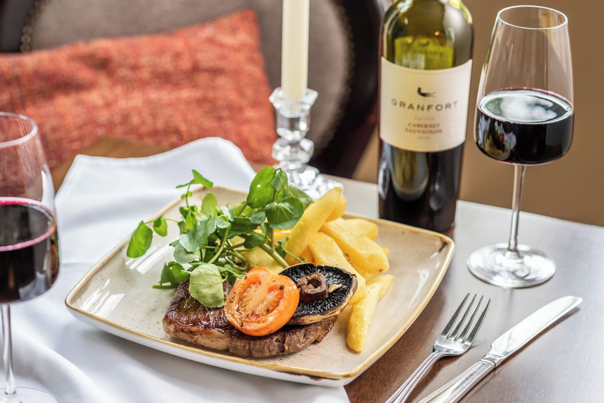 A plate of steak with vegetables and fries, a bottle of wine, and glasses on a table.