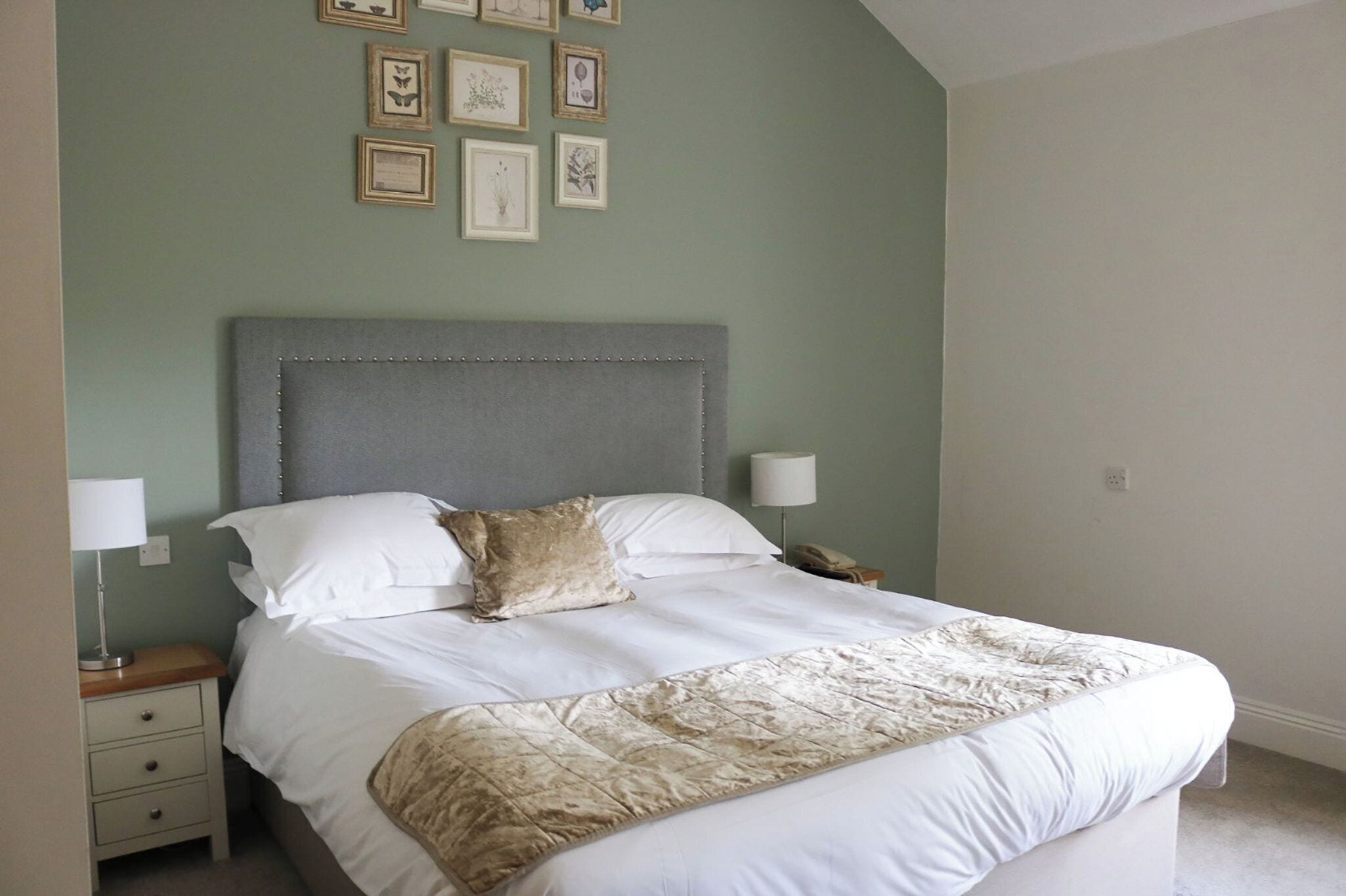 A neatly made bed with white linens and a beige throw blanket, a bedside table with a lamp, and framed artwork on the wall.