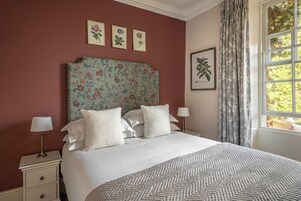 Una cama bien hecha con sábanas blancas y un plaid estampado, cabecera de motivos florales e impresiones botánicas enmarcadas en la pared.