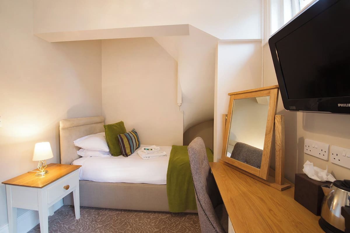 Ein Hotelzimmer mit einem Bett, einem Nachttisch mit Lampe, einem Fernseher und einem Spiegel.