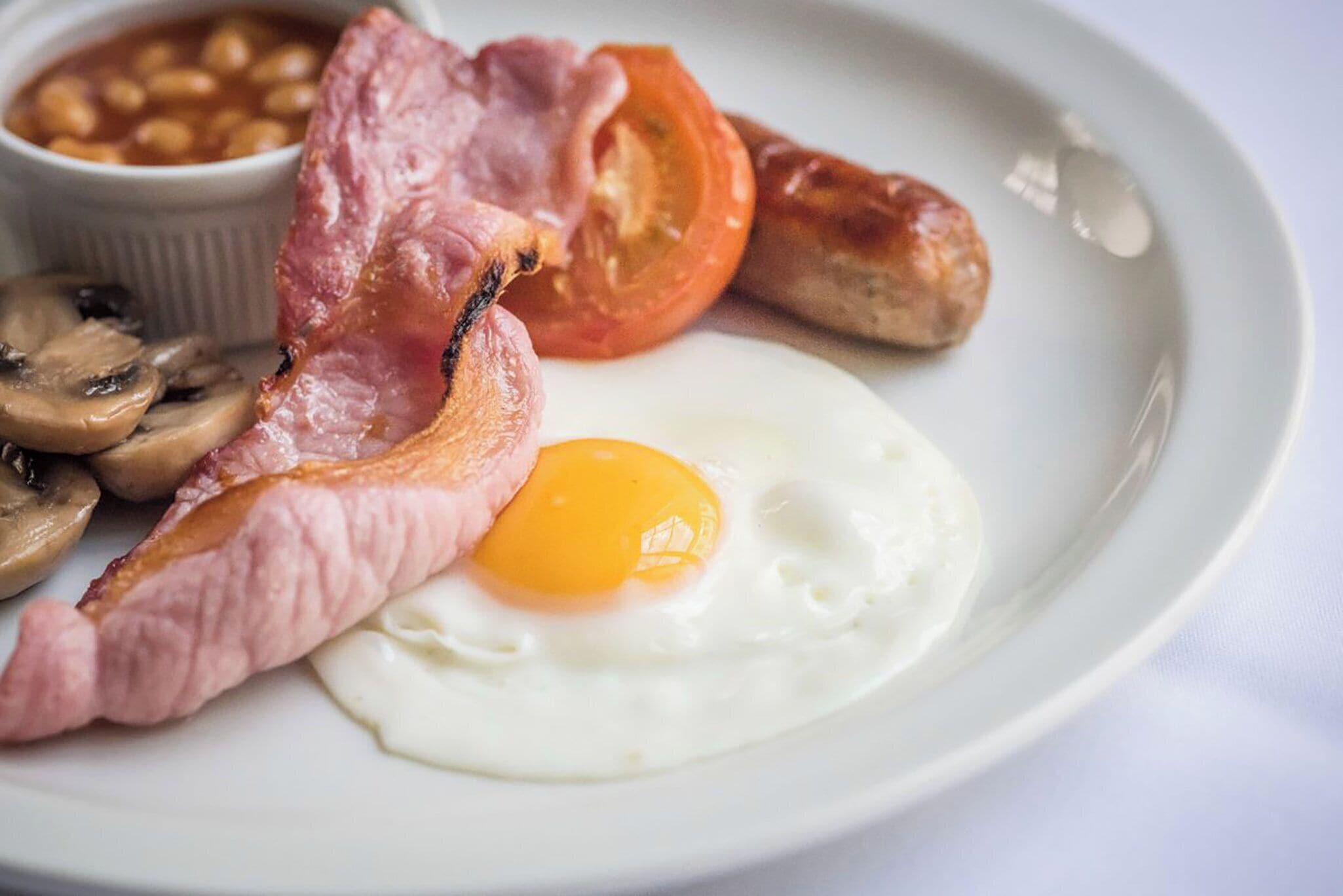 Une assiette composée d’un œuf au plat, de lardons, de saucisses, de champignons et de haricots cuits.
