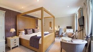 A four-poster bed with a wooden frame, a desk with a chair, a television mounted on the wall, and a small round table with a chair. - Bartley Lodge Hotel (Southampton)