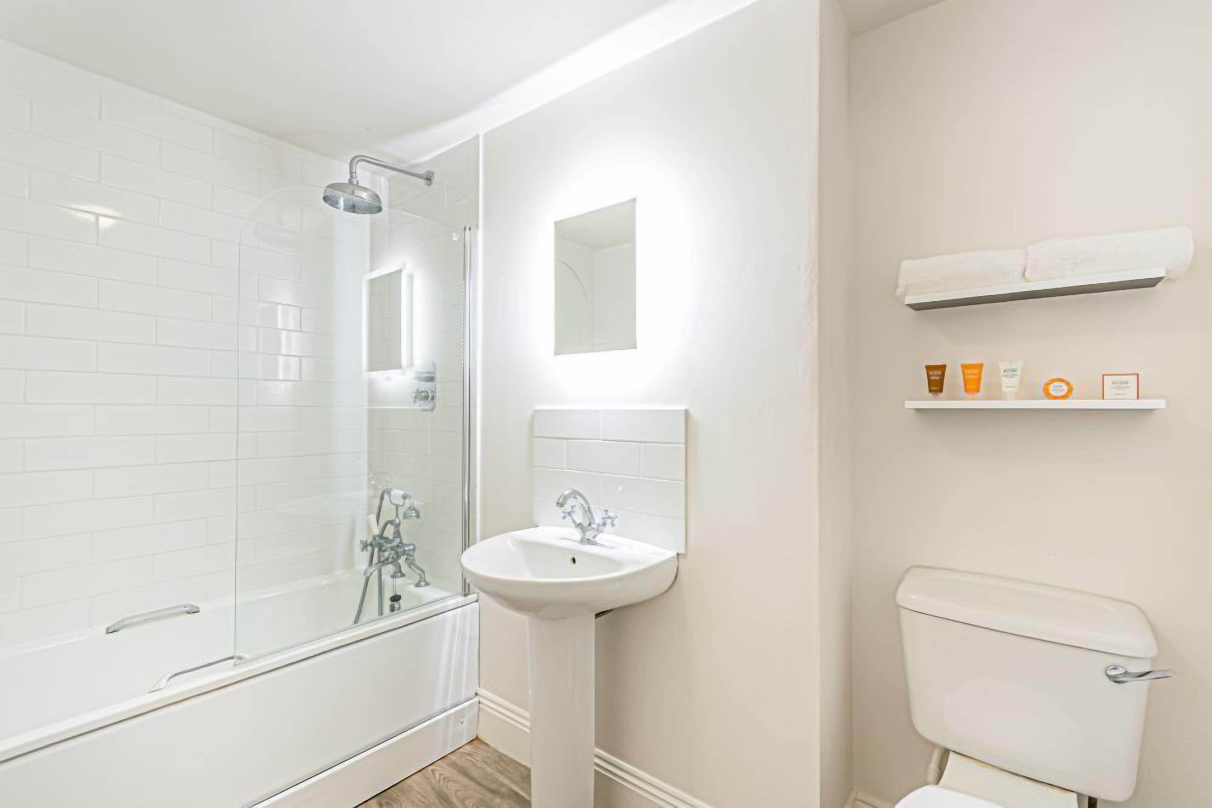 Un bagno moderno con doccia vetro, lavabo a piedistallo e water.