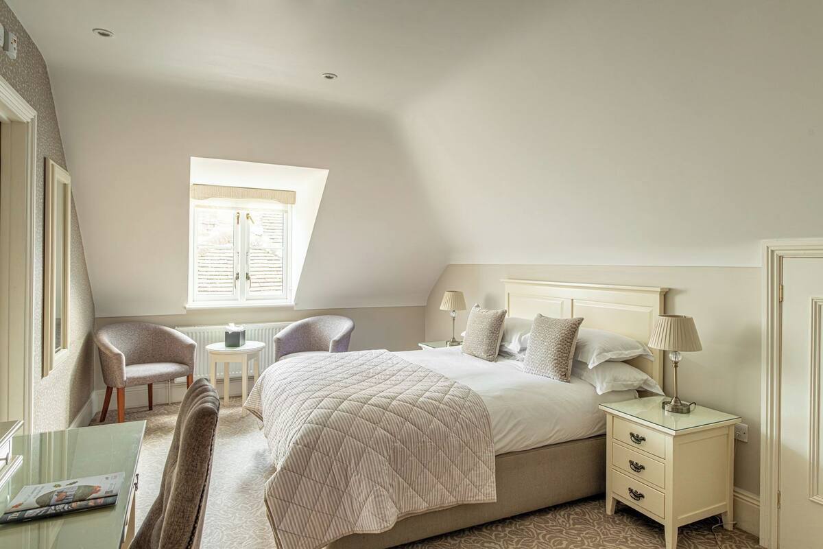 Ein Schlafzimmer mit einem großen Bett, zwei Nachttischen, einem Sessel, einem kleinen Tisch und einem Fenster mit Fensterläden.