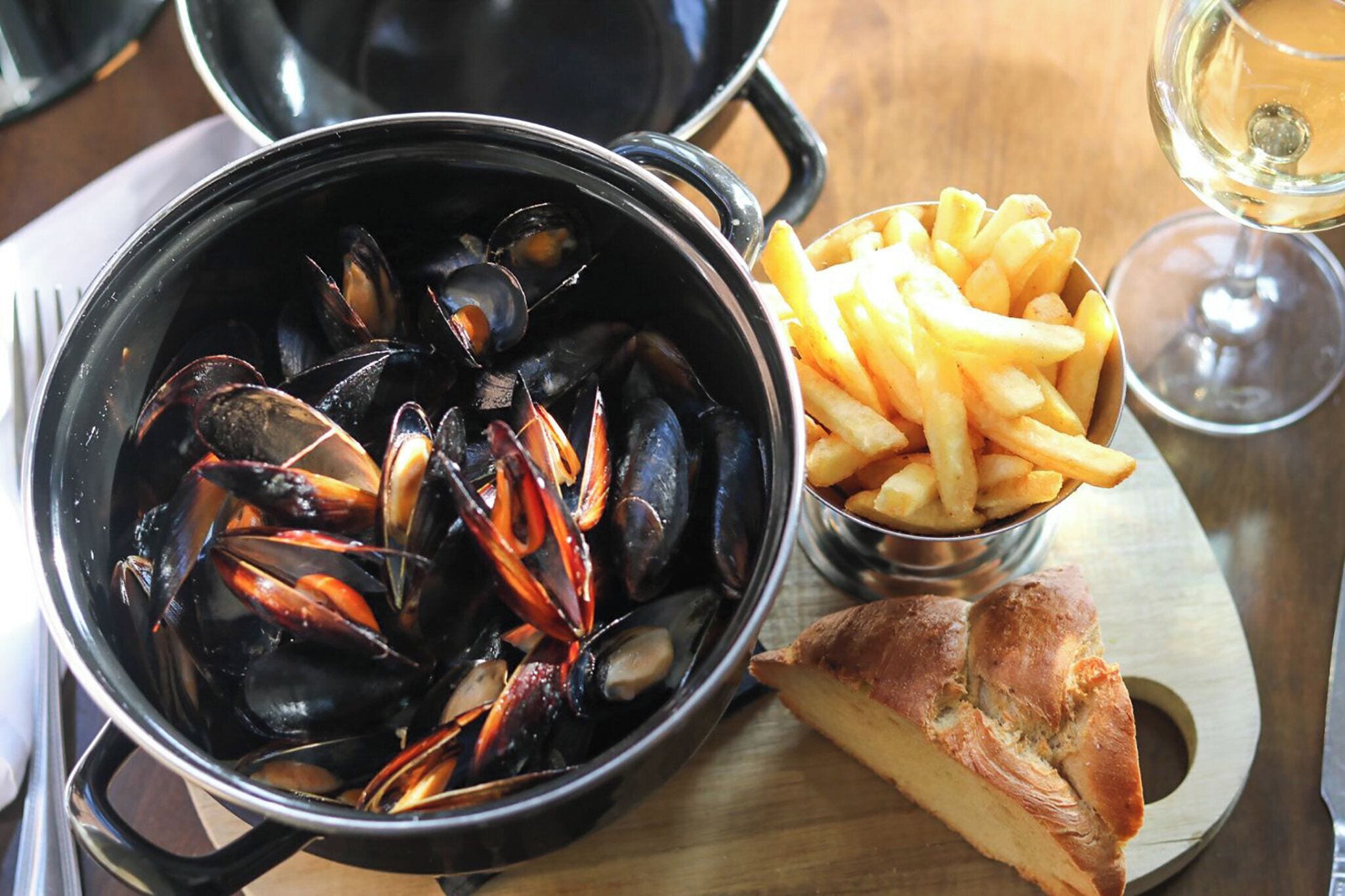Un plato con mejillones, papas fritas y un trozo de pan sobre una tabla de madera.