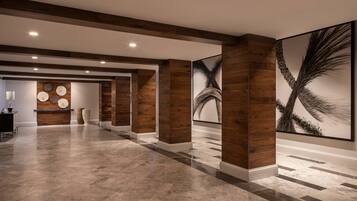 A spacious lobby with a polished marble floor, wooden columns, and large wall art.