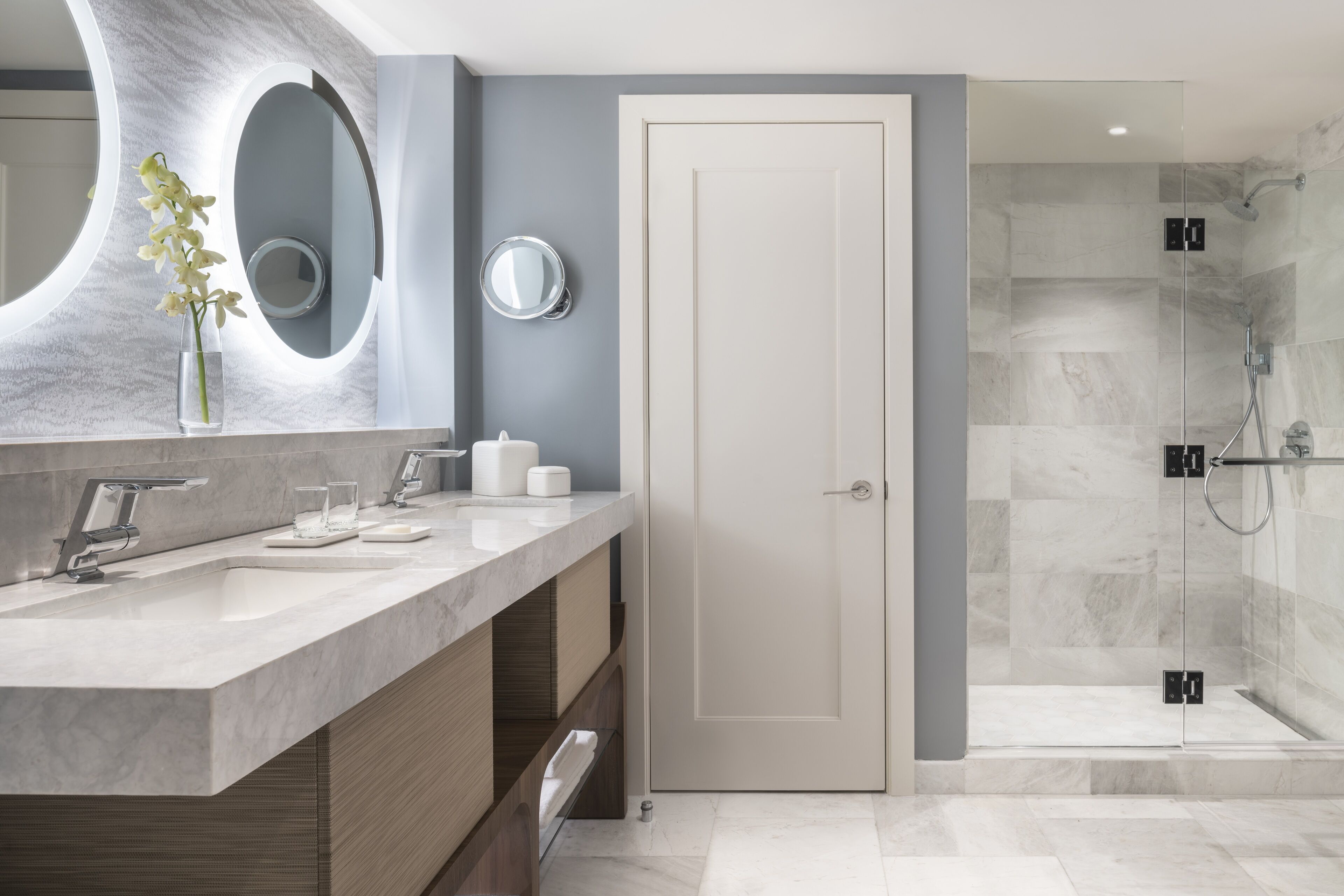 Un baño moderno con tocador de mármol, un espejo grande y zona de ducha.