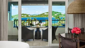 A balcony with a view of a coastal landscape, a round table with chairs, and a vase with flowers.