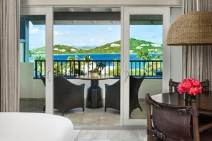 A balcony with a view of a coastal landscape, a round table with chairs, and a vase with flowers.