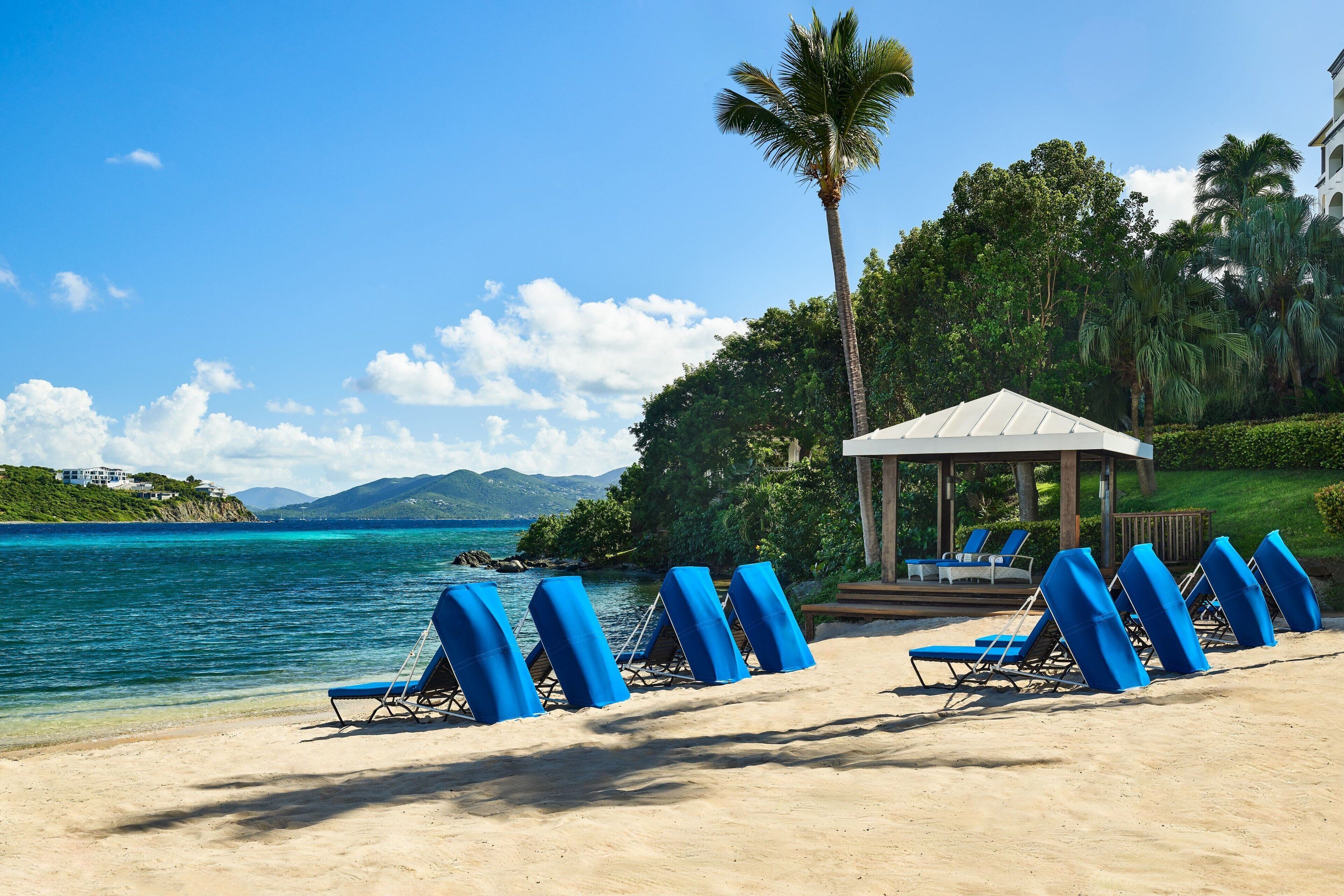 Une plage avec des chaises longues, un kiosque et une vue sur la mer et les montagnes.