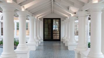 A corridor with white columns and a tiled floor leading to a black door with glass panels.