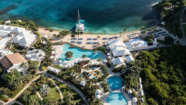 An aerial view of a resort with multiple swimming pools, a beach, and a boat docked near the shore. - The Ritz-Carlton, St. Thomas (St. Thomas)