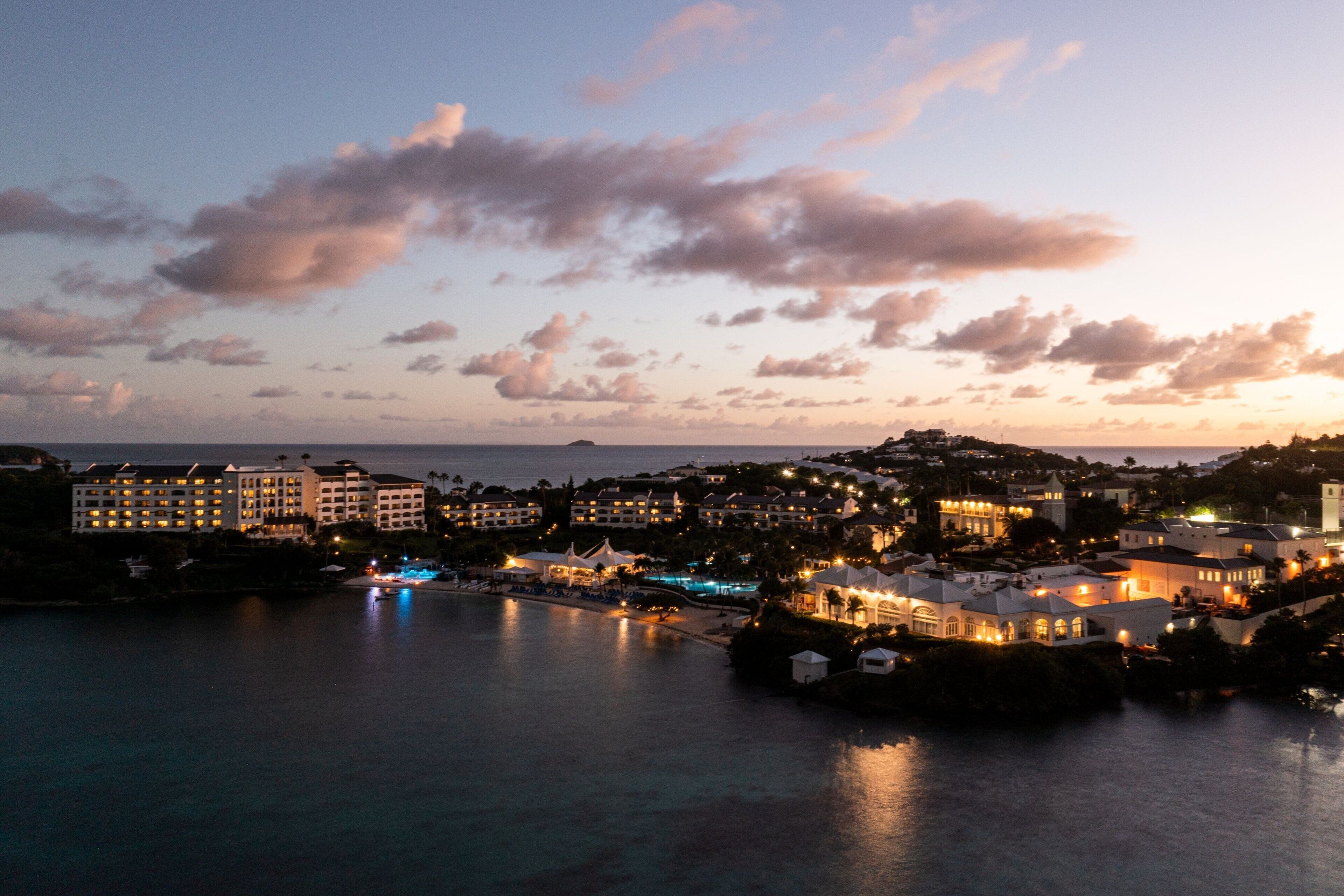 Une ville côtière au crépuscule, avec des bâtiments illuminés et une mer calme.