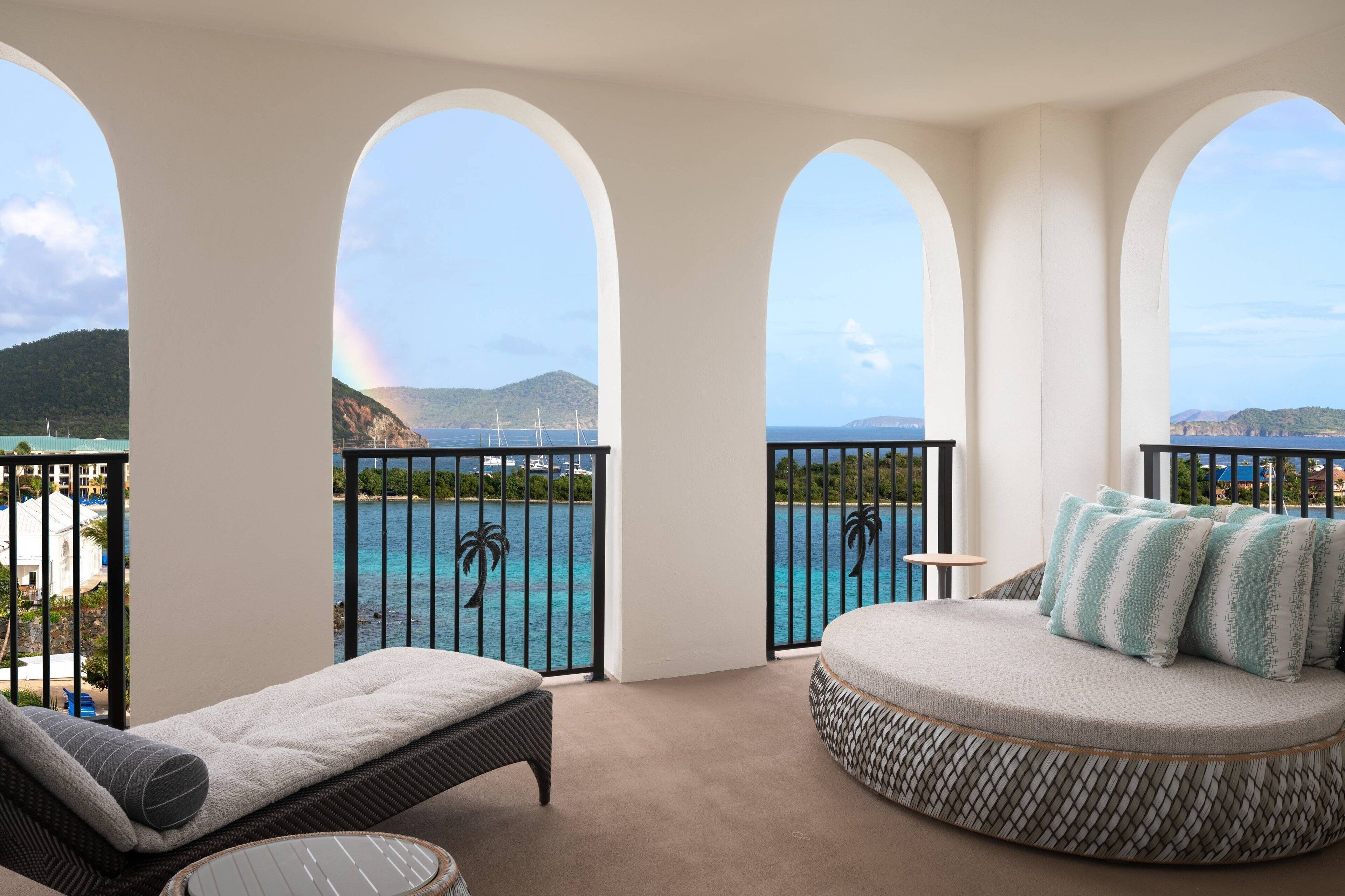 A balcony with a view of the sea and mountains, furnished with a sofa and a chair.