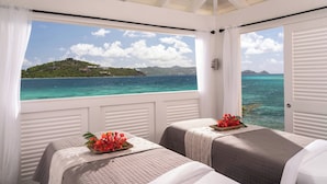 A room with two beds, a view of the ocean, and a balcony with white railings.