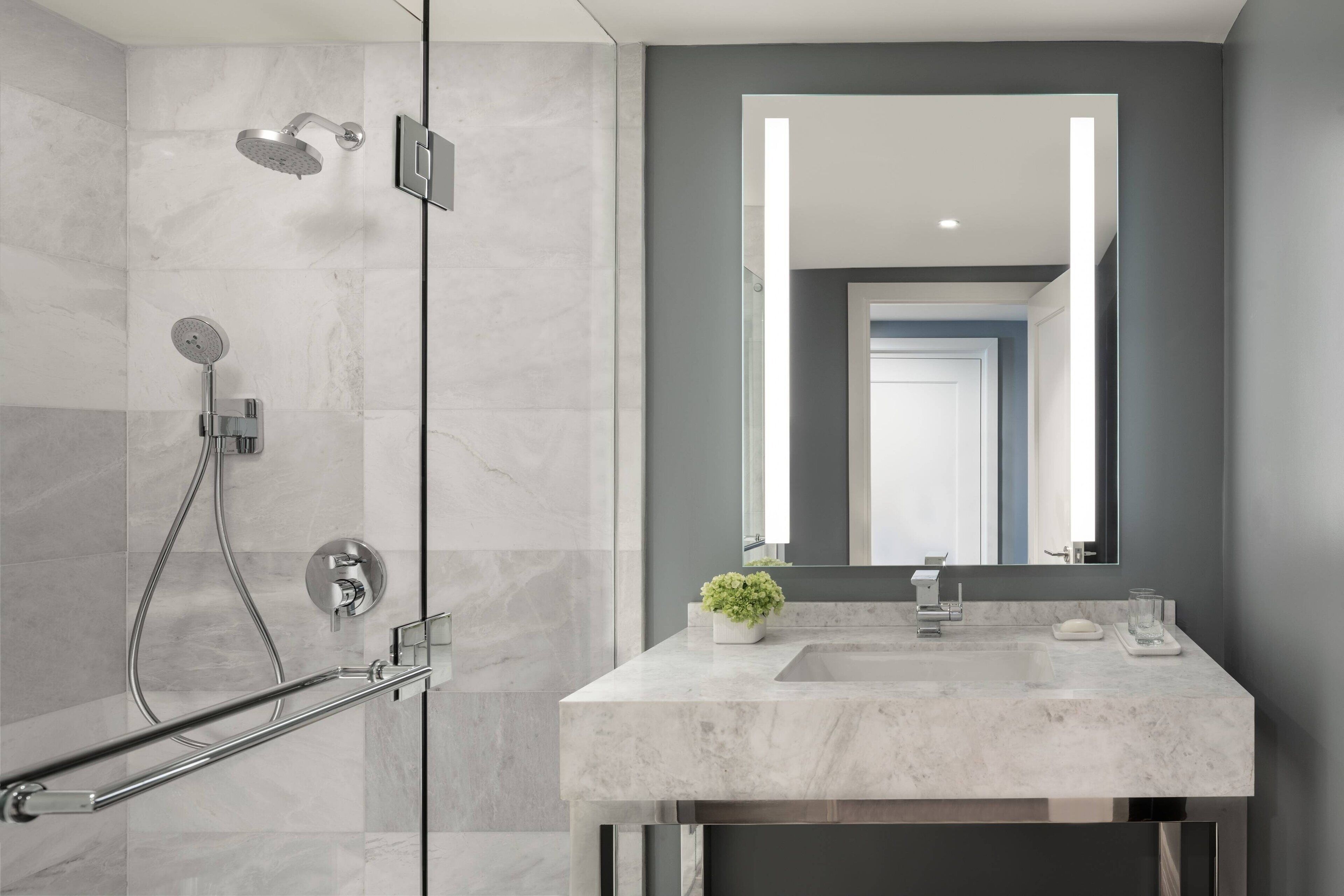 Une salle de bain moderne avec une douche à l’italienne en verre, un lavabo en marbre et un grand miroir.
