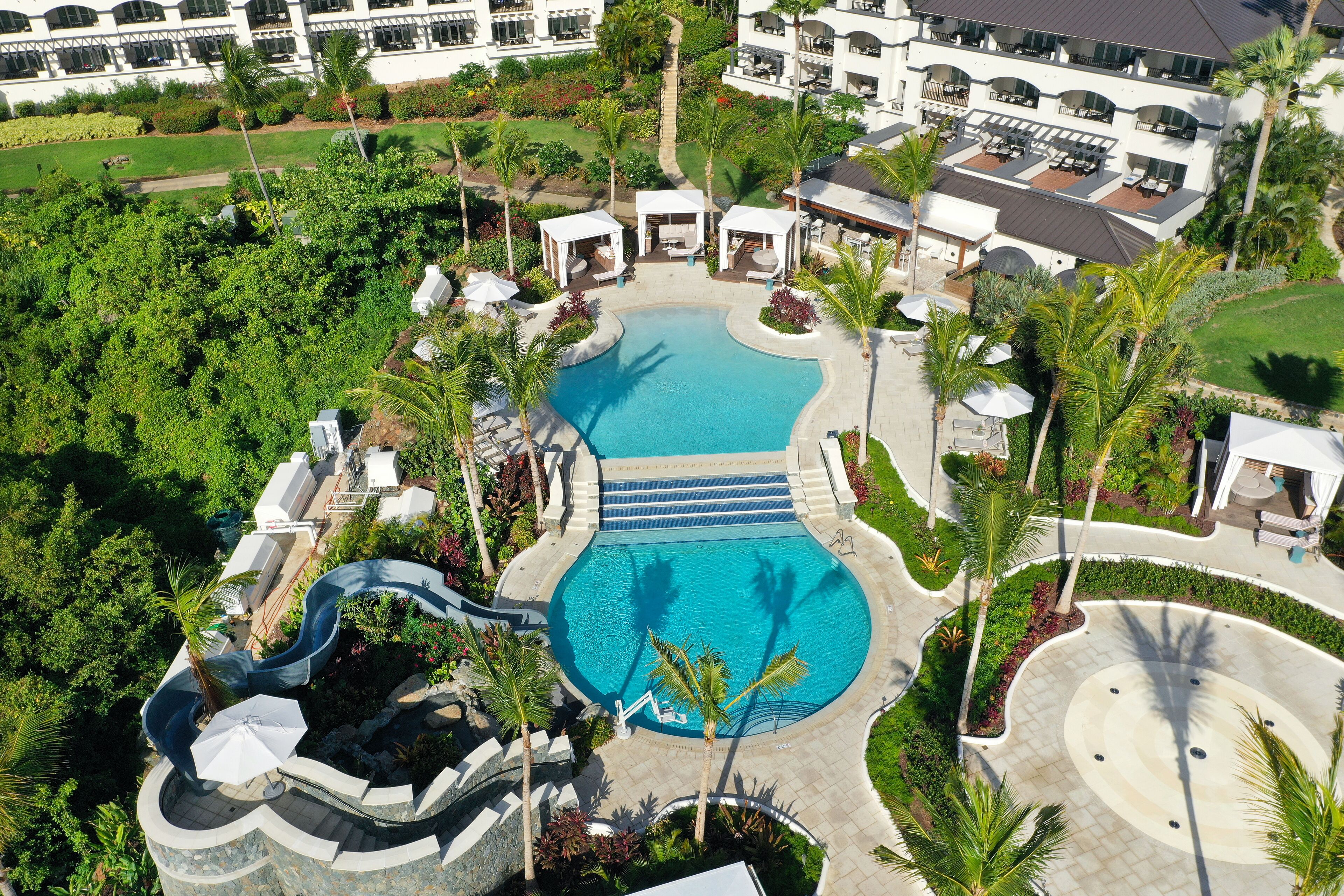 An aerial view of a resort with a central swimming pool, lounge areas, and a waterfall feature.