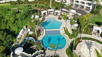 Vista aérea de un resort con piscina central, zonas de descanso y una cascada.